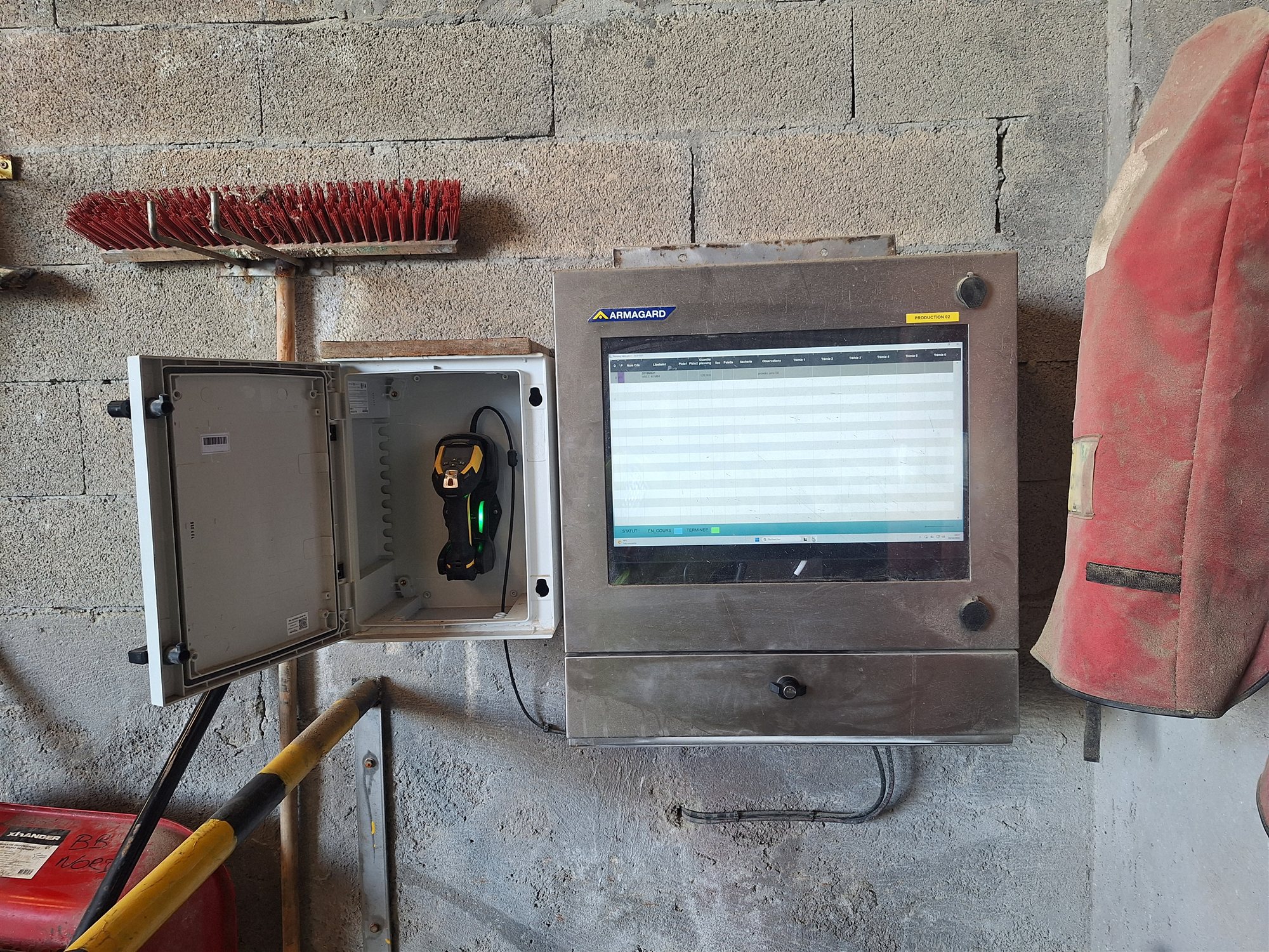 Poste de production digitalisé : écran du planning de fabrication dans un coffret inox et scanette prête à l'emploi dans son boîtier mural