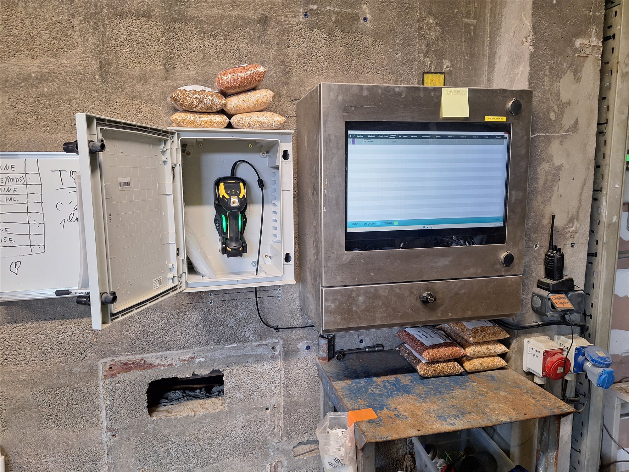 Écran du planning de fabrication installé dans l'atelier, avec la scanette utilisée pour les saisies de production à portée de main